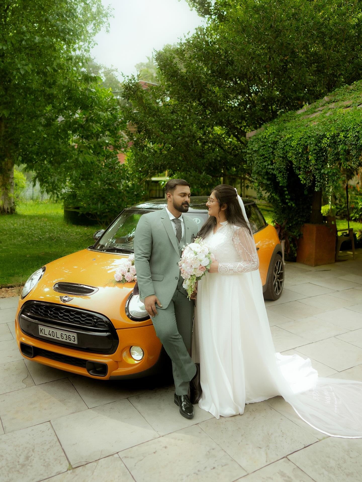 A newlywed couple posing beside an orange car